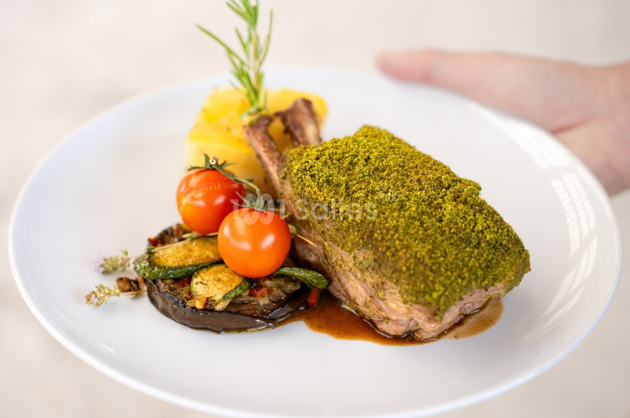 Carré d'agneau en croûte d'herbes servi avec légumes grillés, tomates cerises et gratin de pommes de terre.