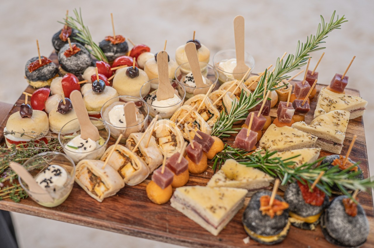 Plateau en bois garni de divers amuse-bouches salés et sucrés, décoré de branches de romarin.