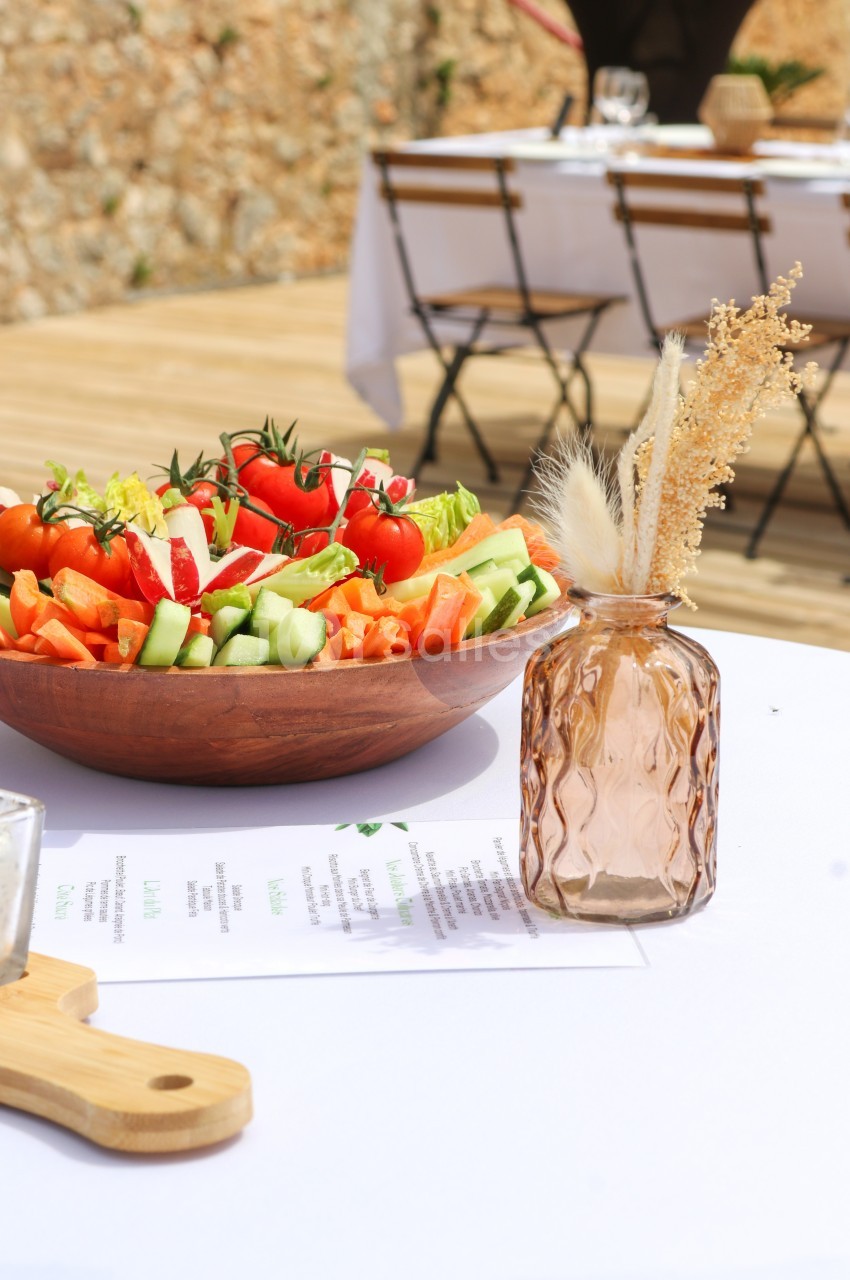 Salade de légumes frais dans un bol en bois sur une table extérieure, avec un vase décoratif et des chaises en arrière-plan.
