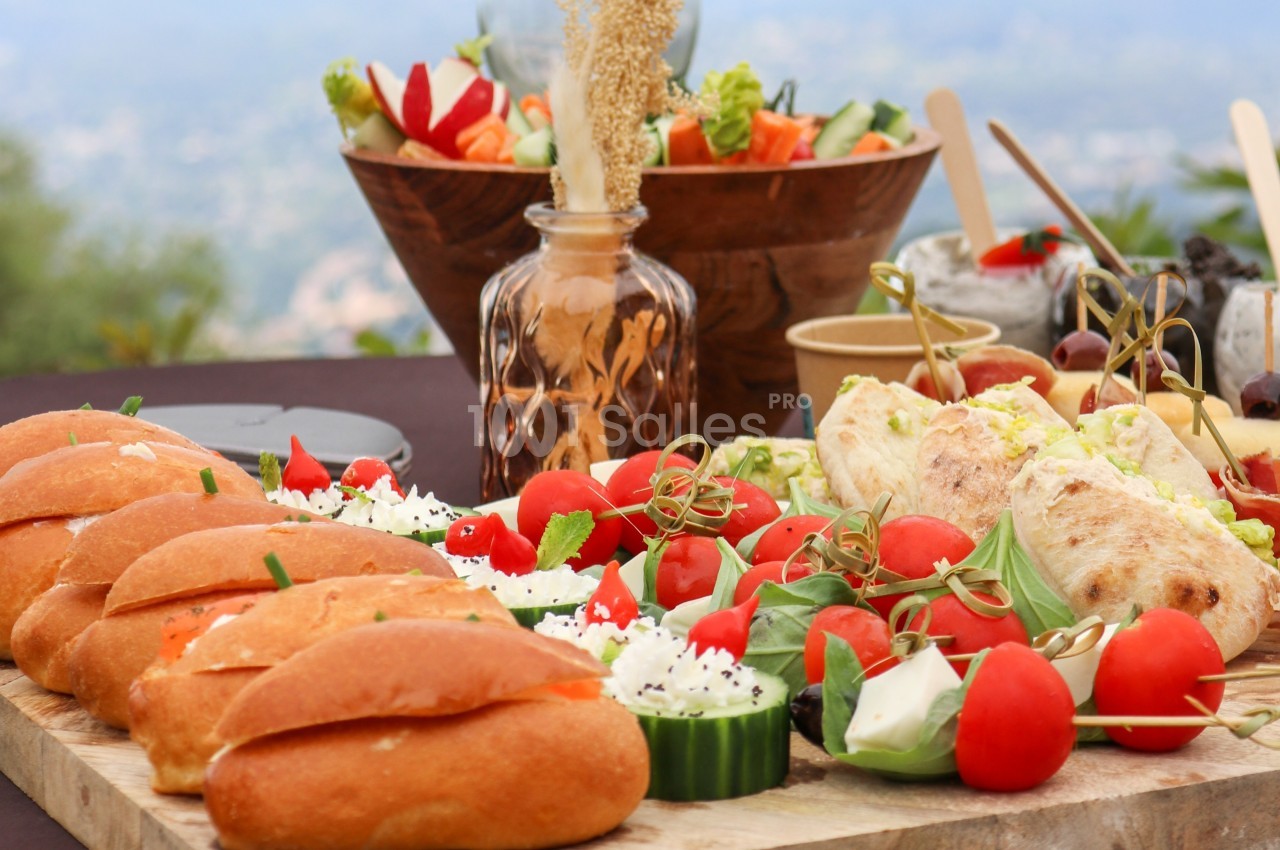 Plateau de buffet avec sandwichs, légumes frais, tomates cerises, fromage et desserts en arrière-plan.