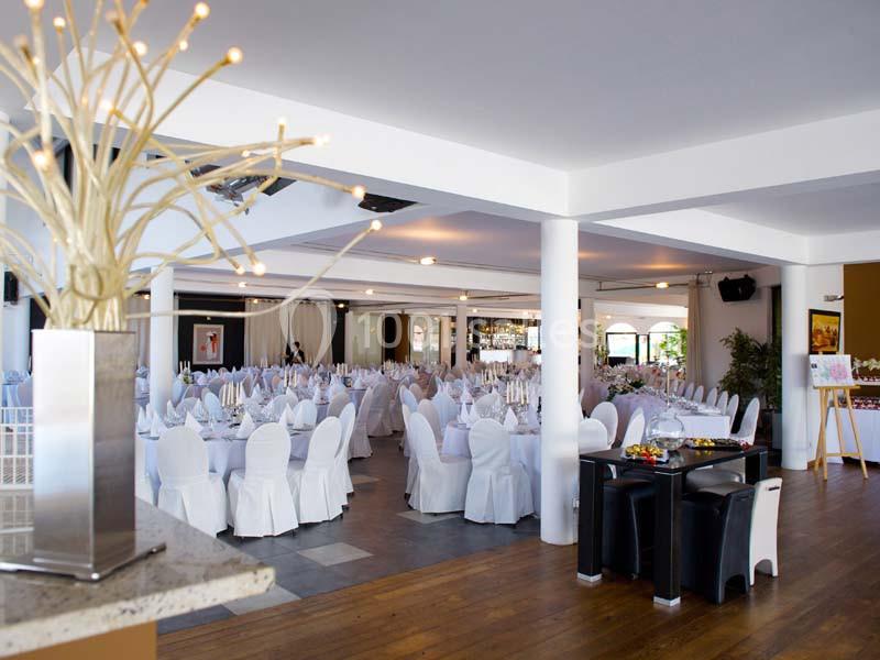 Salle de réception lumineuse avec tables rondes dressées de nappes blanches et chaises assorties.