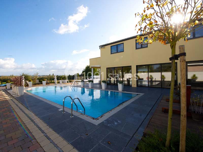 Piscine extérieure entourée de dalles grises, près d'une maison moderne avec de grandes baies vitrées.