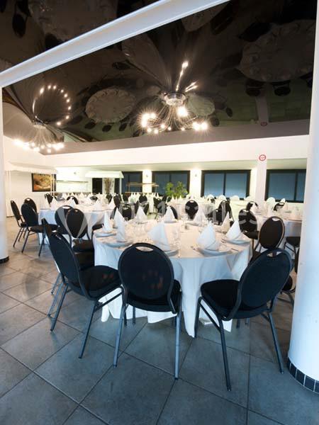 Salle de réception avec tables rondes dressées de nappes blanches, serviettes pliées et chaises noires.
