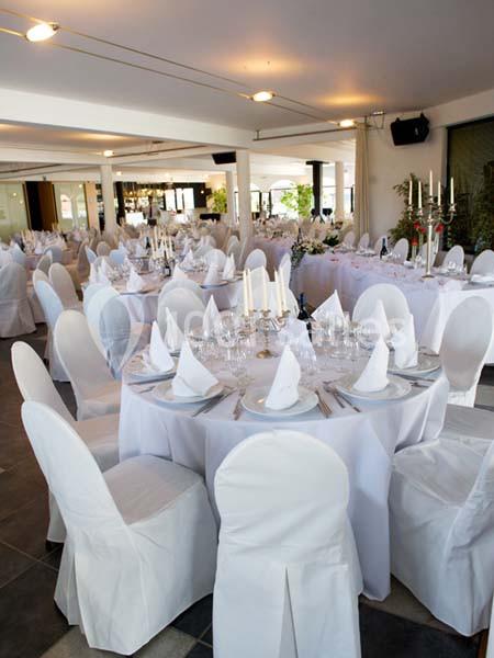 Salle de réception élégamment décorée avec des tables rondes, nappes blanches, serviettes pliées et chandeliers.