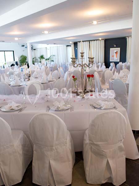 Salle de réception décorée avec des tables rondes et rectangulaires, nappes blanches et chandeliers argentés.