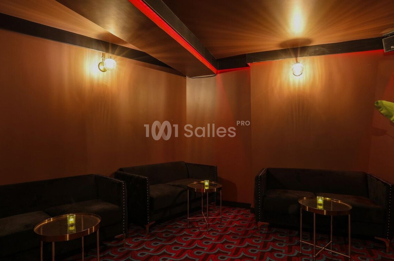 Salle au décor chaleureux avec murs marron, canapés noirs, tables basses dorées et éclairage tamisé.