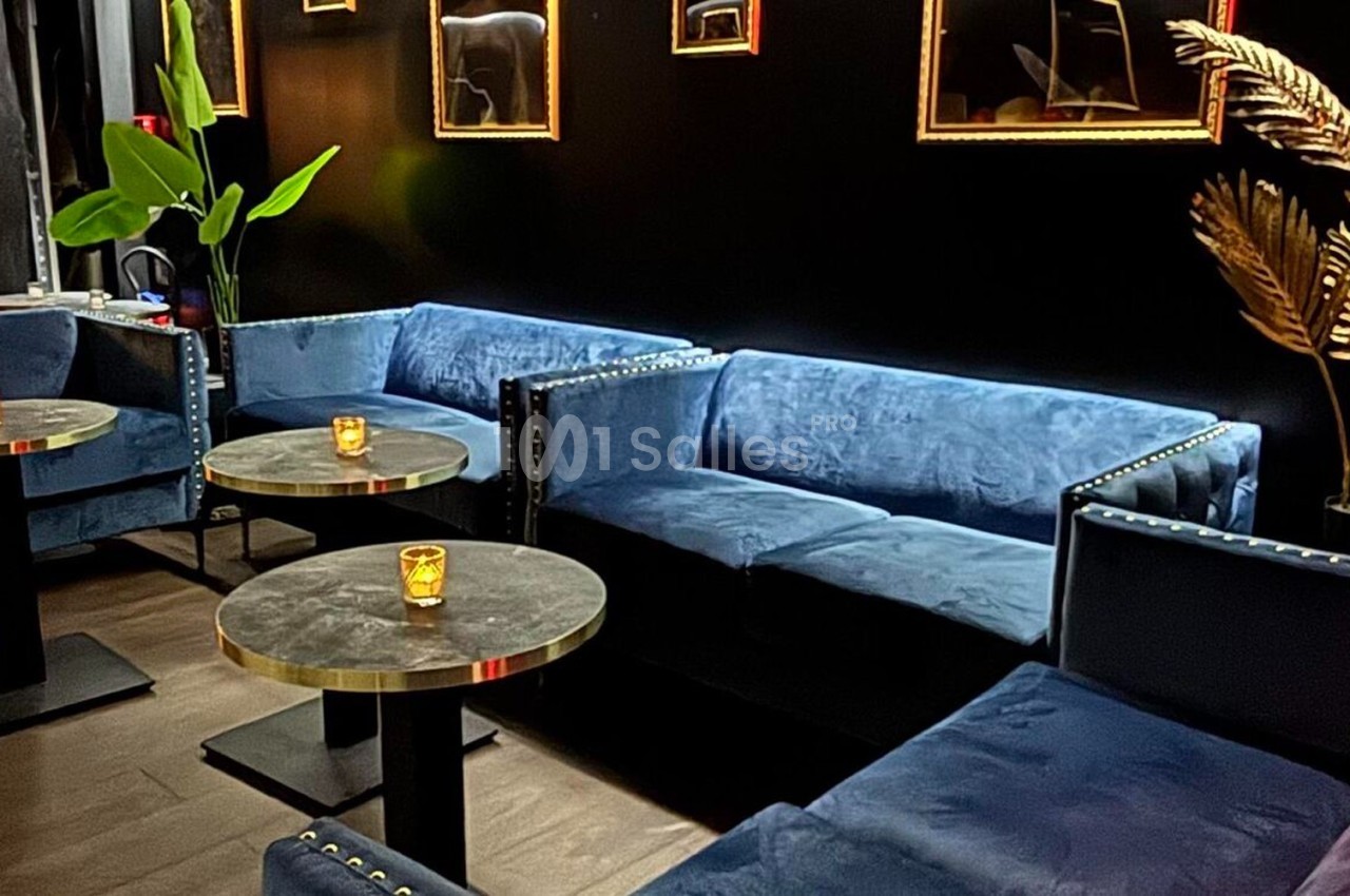 Canapés bleus en velours entourant des tables rondes noires avec bougies, dans un intérieur sombre et élégant.