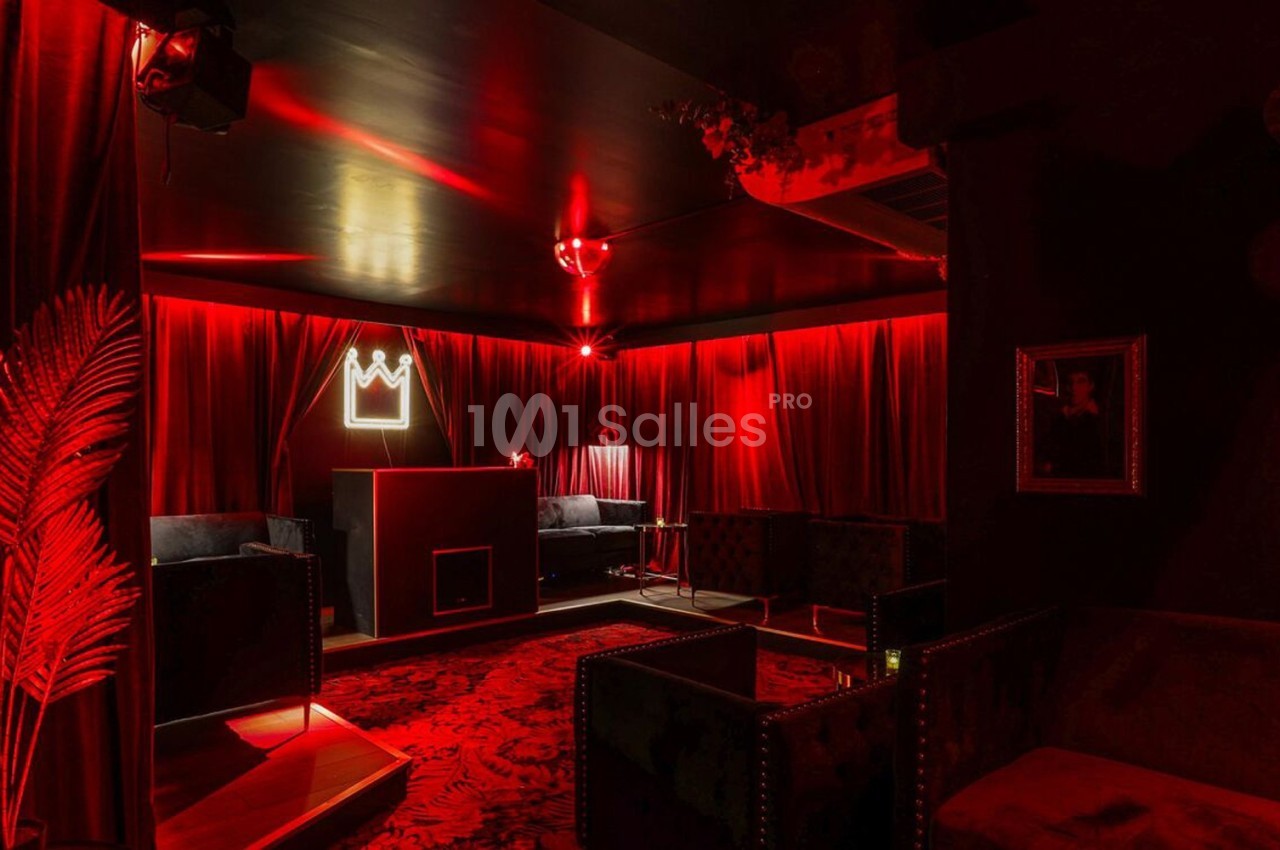 Salle lounge avec éclairage rouge tamisé, fauteuils sombres, rideaux en velours et décoration murale minimaliste.