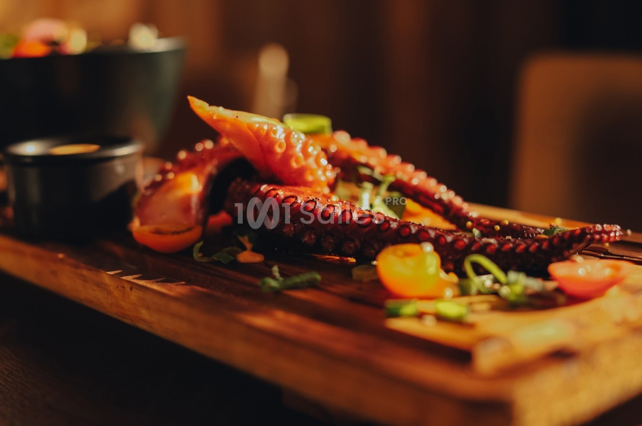 Tentacules de poulpe grillés servis sur une planche en bois avec légumes et herbes en garniture.