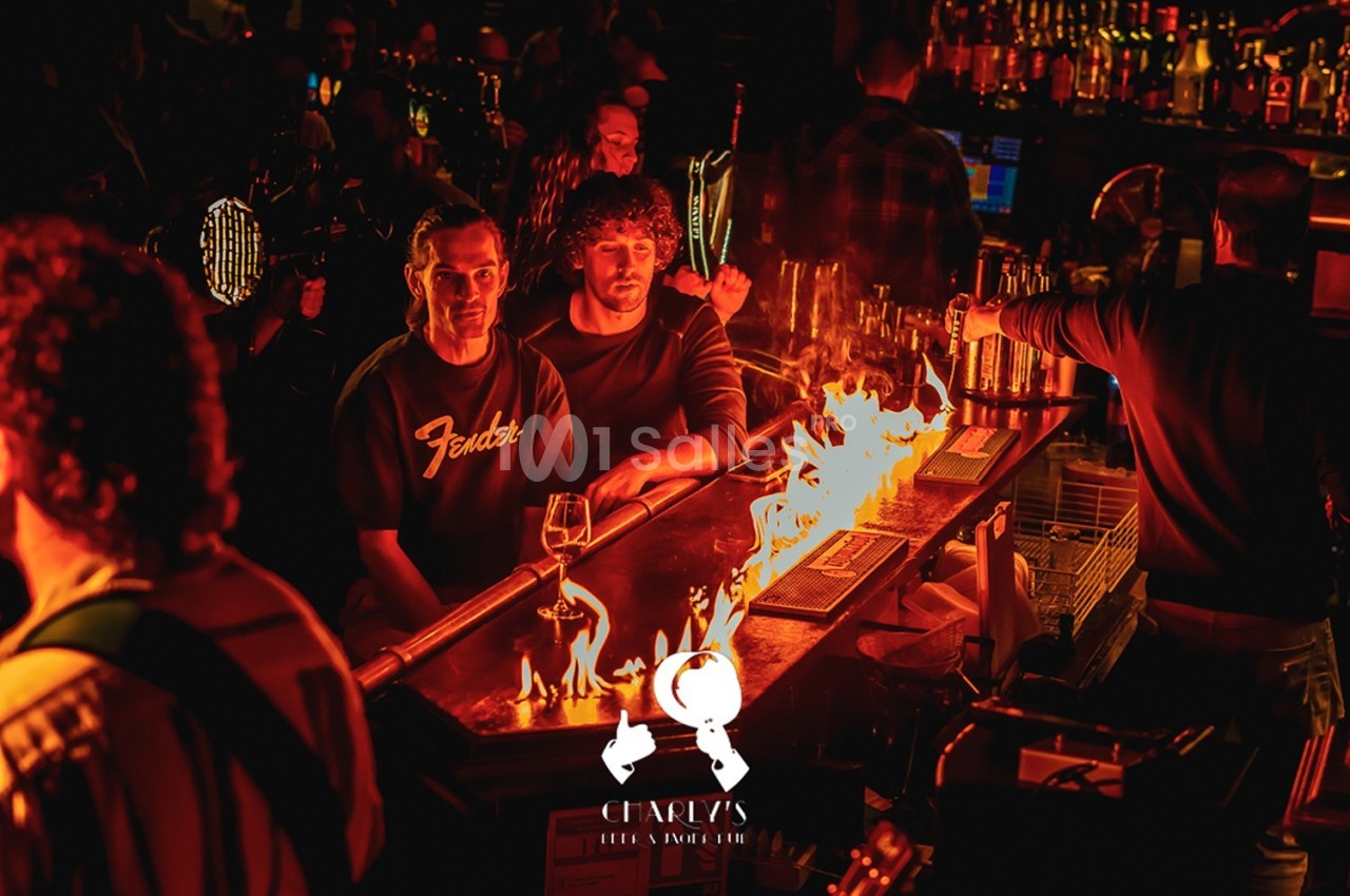 Des clients assis au bar regardent un comptoir enflammé dans une ambiance de bar animée et tamisée.