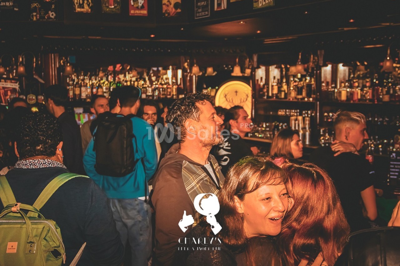 Des personnes discutent et s'amusent dans un bar animé, avec un comptoir rempli de bouteilles en arrière-plan.