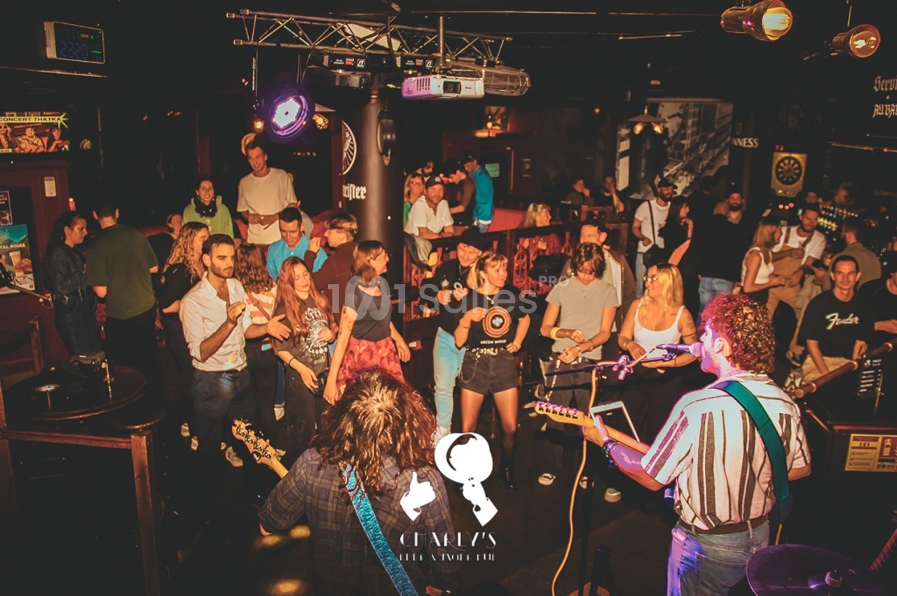 Un groupe de musiciens joue sur scène dans un bar animé, avec un public dansant et applaudissant.