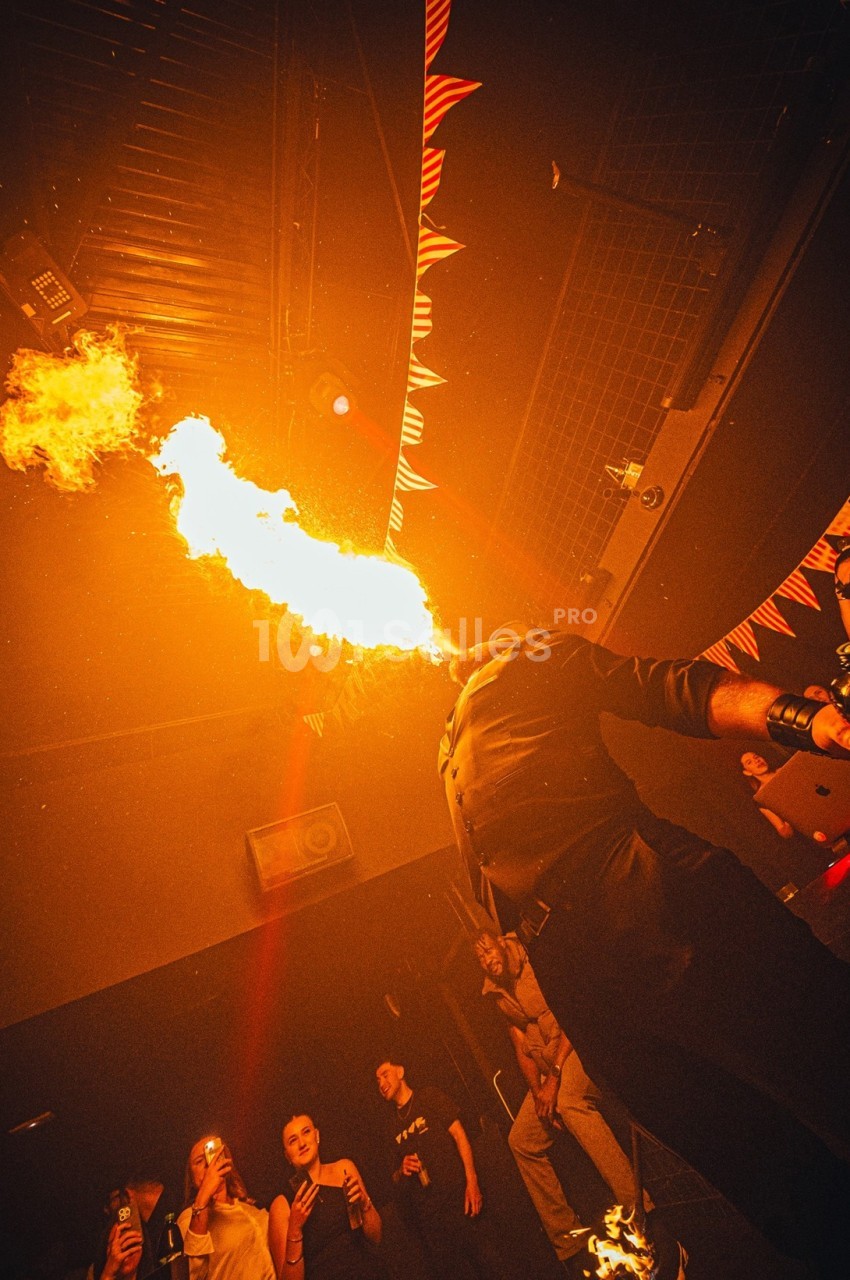 Un artiste cracheur de feu performe devant un public dans une ambiance sombre et festive.