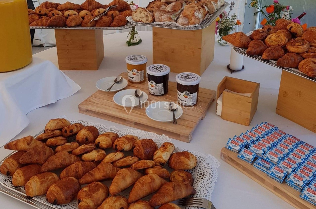 Plateau de viennoiseries variées avec confitures, jus d'orange et décorations florales sur une table blanche.