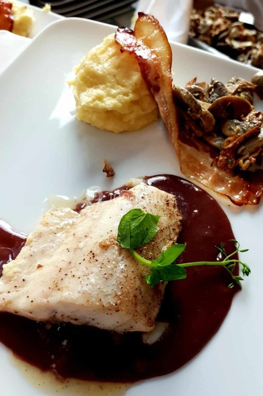 Filet de poisson nappé de sauce brune, accompagné de purée, lard croustillant et légumes sautés.
