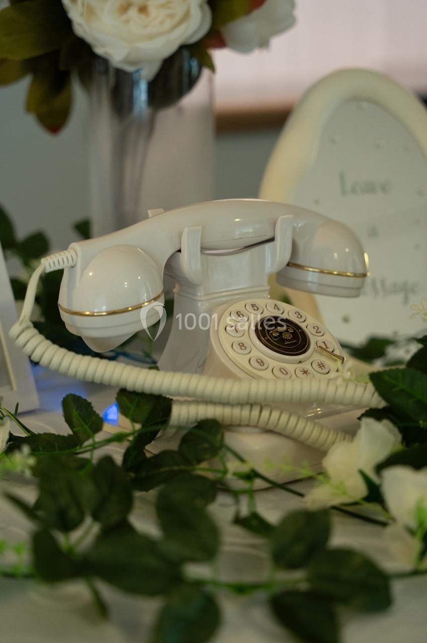 Téléphone vintage blanc avec cadran rotatif, entouré de fleurs et de verdure sur une table décorative.