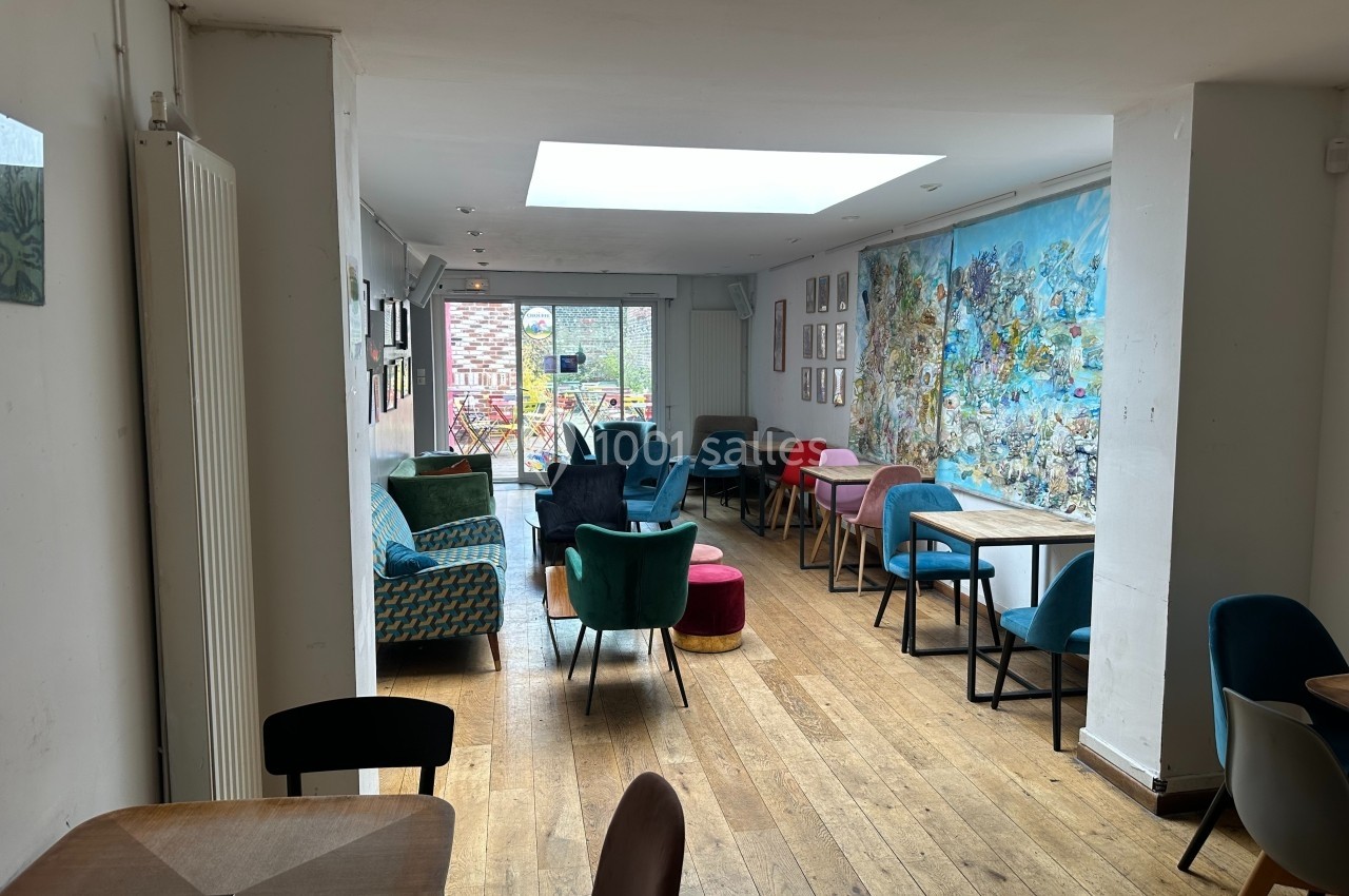 Salle lumineuse avec parquet, mobilier coloré et fresque murale, donnant sur une terrasse avec vue extérieure.