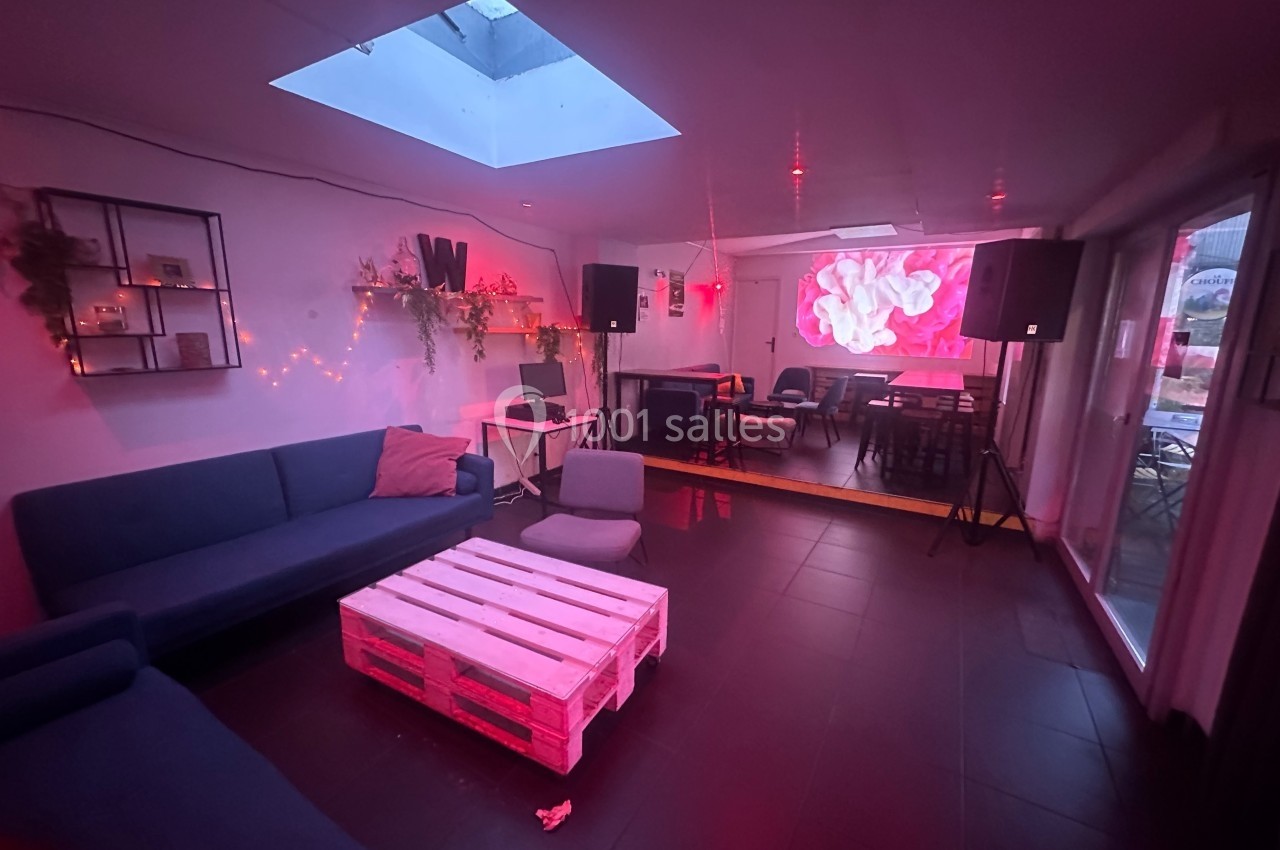 Salle avec canapé, table basse en palette, éclairage rouge tamisé, écran mural et décoration végétale.