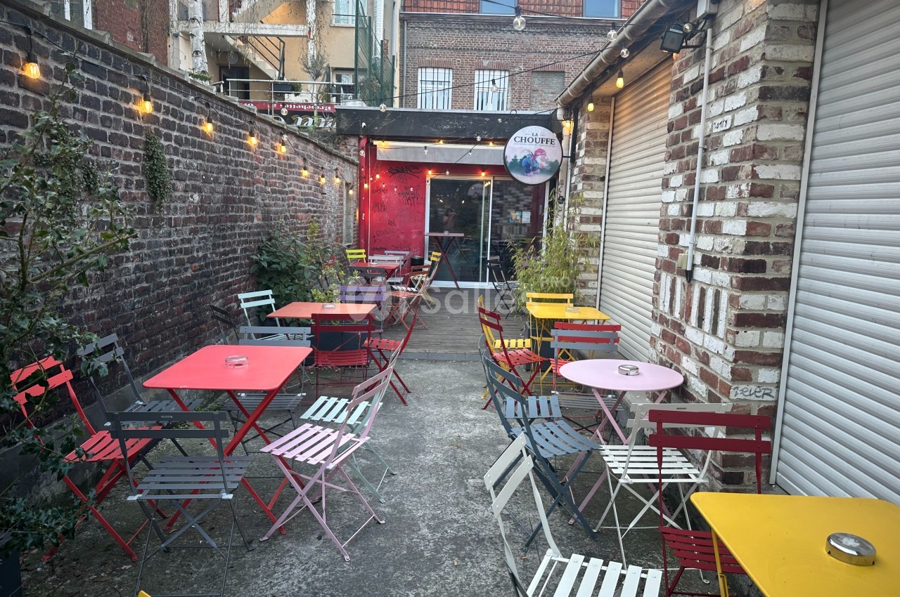 Terrasse extérieure avec tables et chaises colorées, entourée de murs en briques et éclairée par des guirlandes lumineuses.