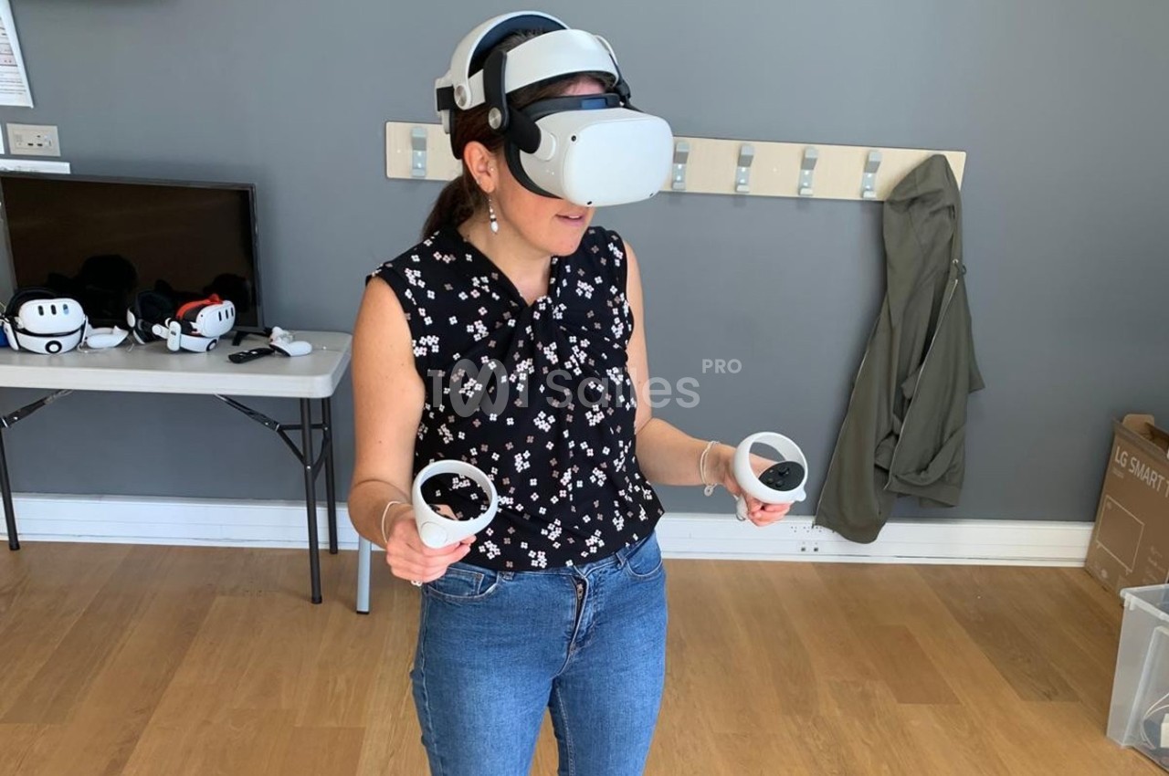 Femme utilisant un casque de réalité virtuelle avec des manettes dans une pièce au sol en bois.