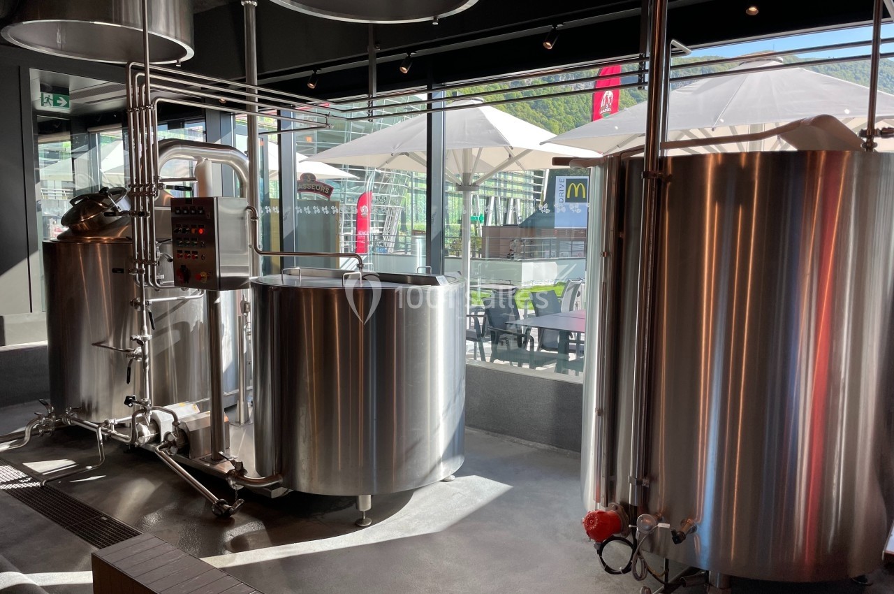 Cuves en acier inoxydable dans une brasserie artisanale, avec vue sur une terrasse extérieure ensoleillée.