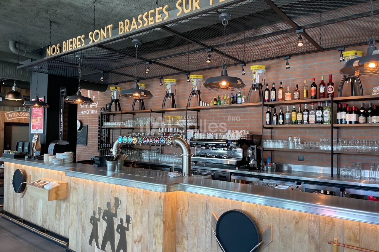 Comptoir de bar moderne avec tireuses à bière, étagères de bouteilles et enseigne ’Nos bières sont brassées sur place’.