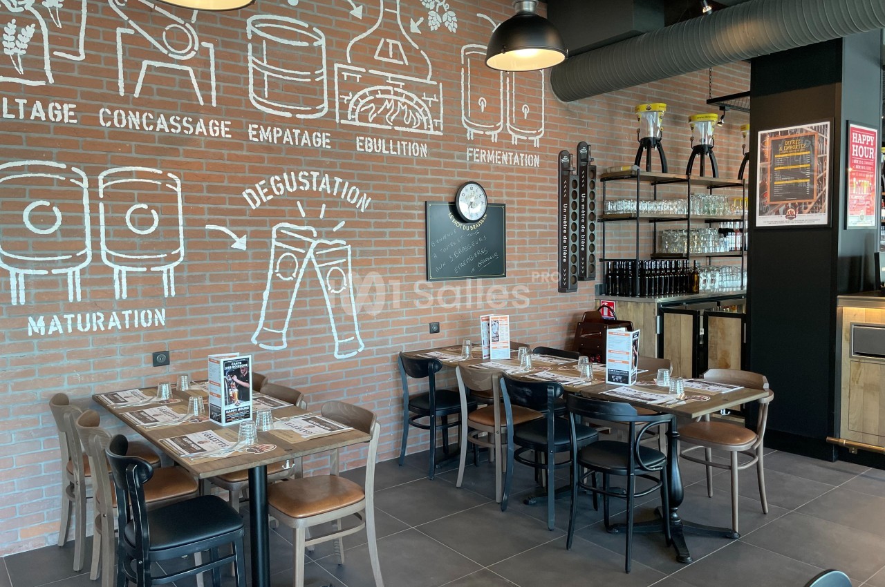 Salle de restaurant avec tables dressées, mur en briques décoré de schémas sur le processus de fabrication de la bière.