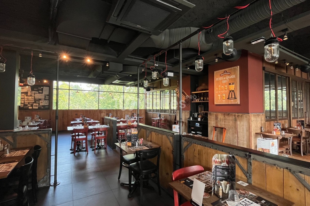 Salle de restaurant avec tables en bois, chaises rouges et noires, éclairage suspendu et grandes fenêtres donnant sur l…