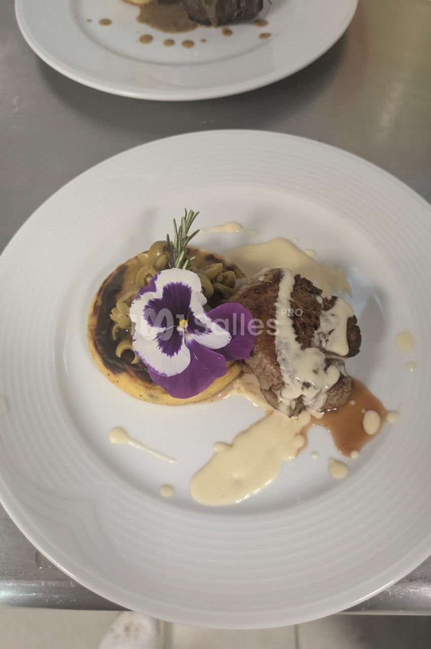 Assiette gastronomique avec viande, purée, sauce crémeuse, champignons et décoration florale comestible.