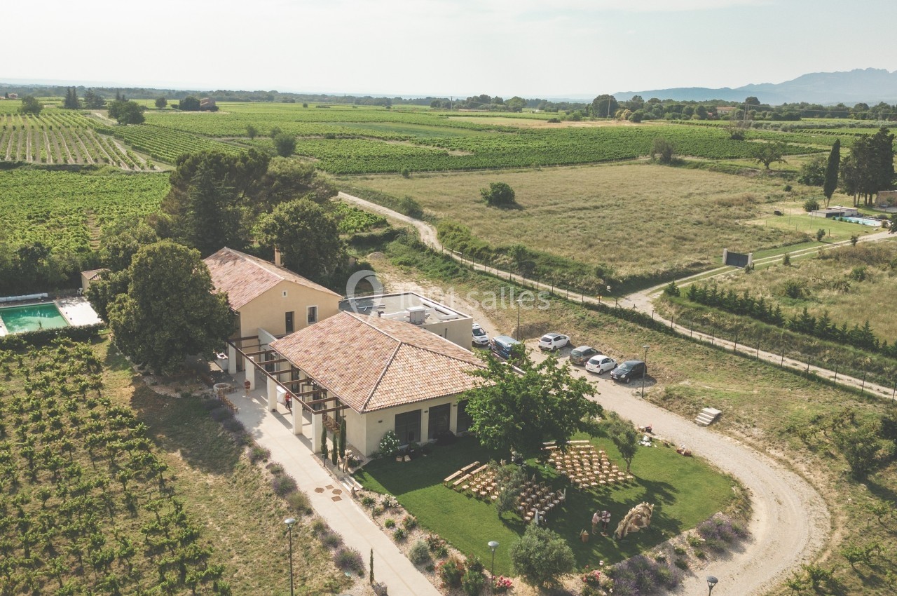 Vue aérienne d'une maison entourée de vignes et de champs, avec une piscine et des voitures stationnées à proximité.