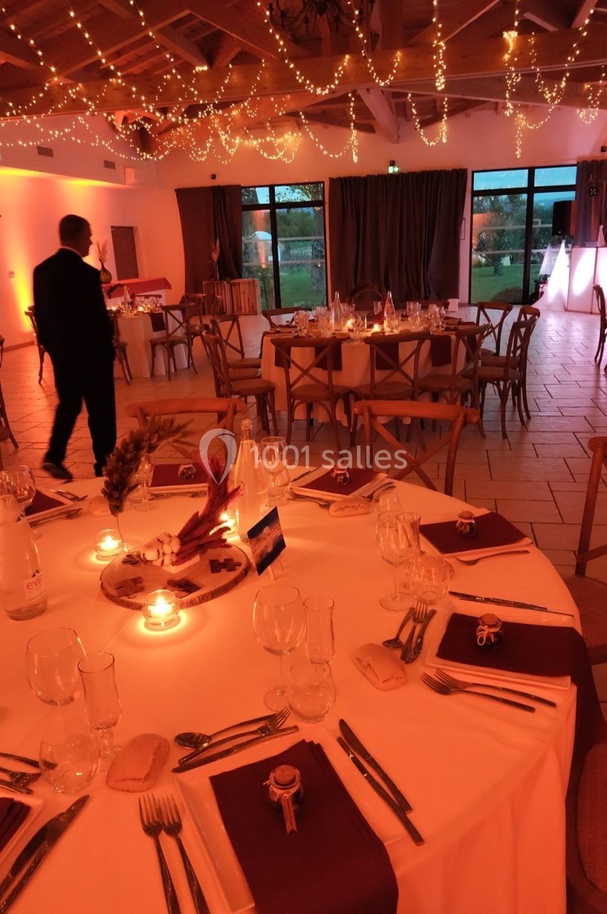 Salle de réception décorée avec des guirlandes lumineuses, tables rondes dressées et ambiance chaleureuse.