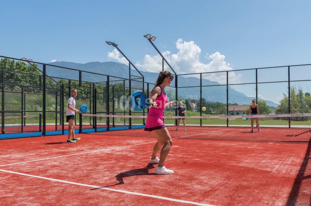 Quatre personnes jouent au padel sur un court extérieur avec vue sur des montagnes et un ciel dégagé.