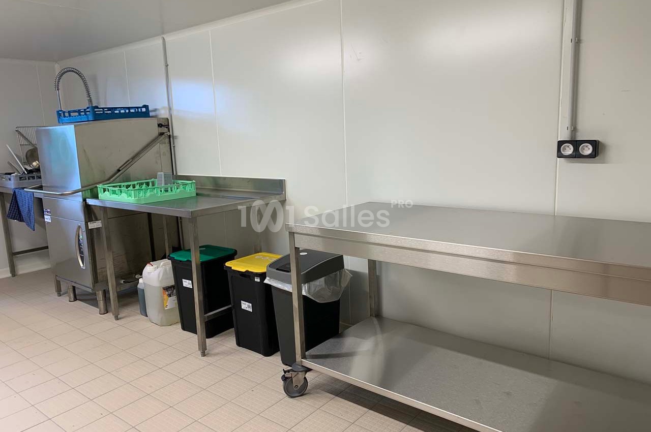 Cuisine professionnelle avec plans de travail en inox, lave-vaisselle industriel, poubelles triées et sol carrelé.