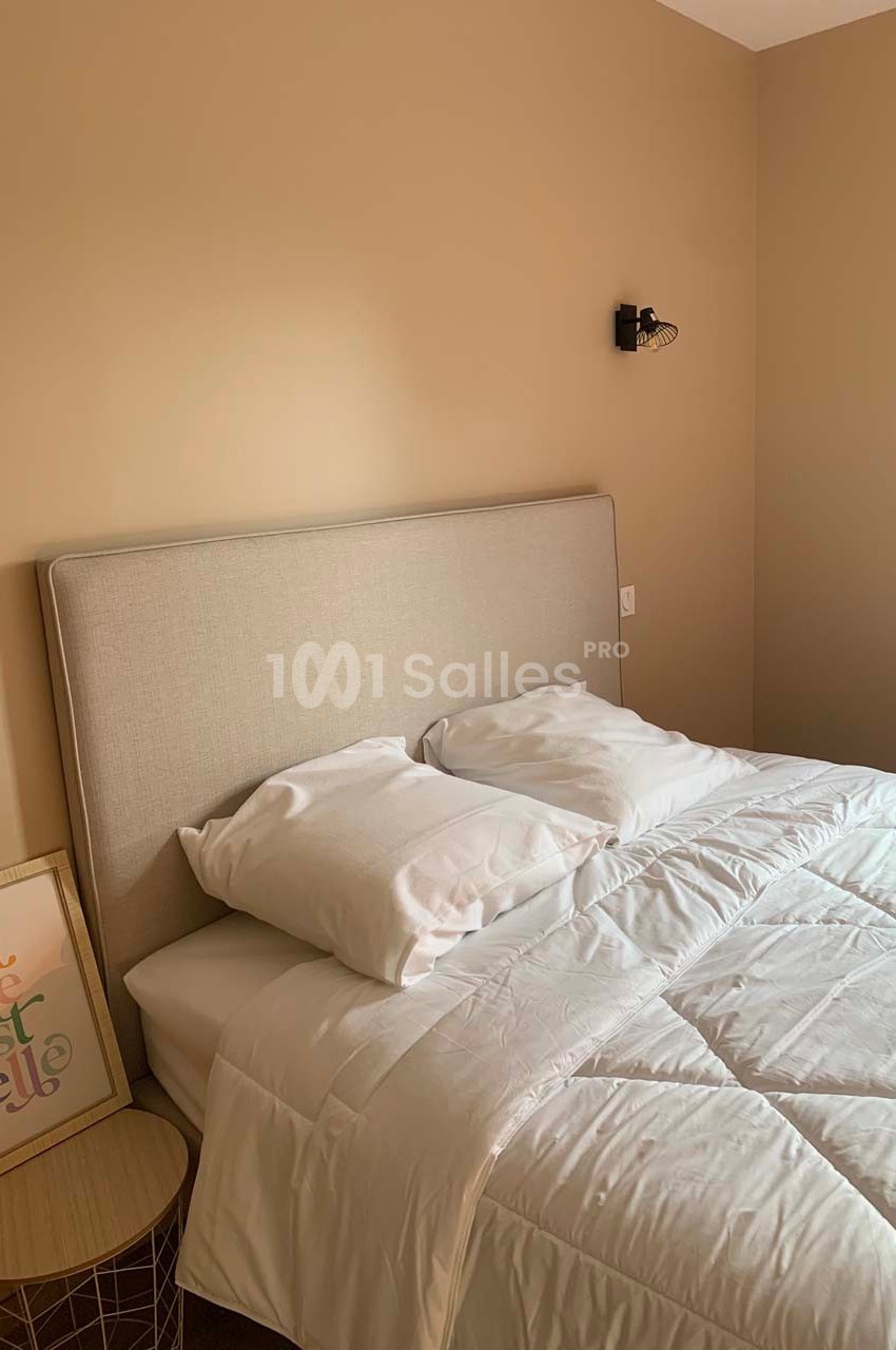 Lit double avec tête de lit beige, draps blancs, table de chevet en bois et cadre décoratif dans une chambre beige.