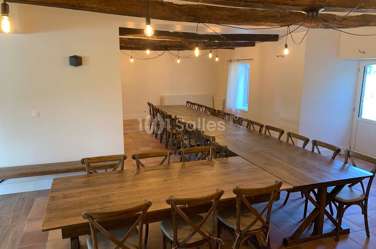 Salle lumineuse avec de longues tables en bois, chaises assorties et poutres apparentes au plafond.