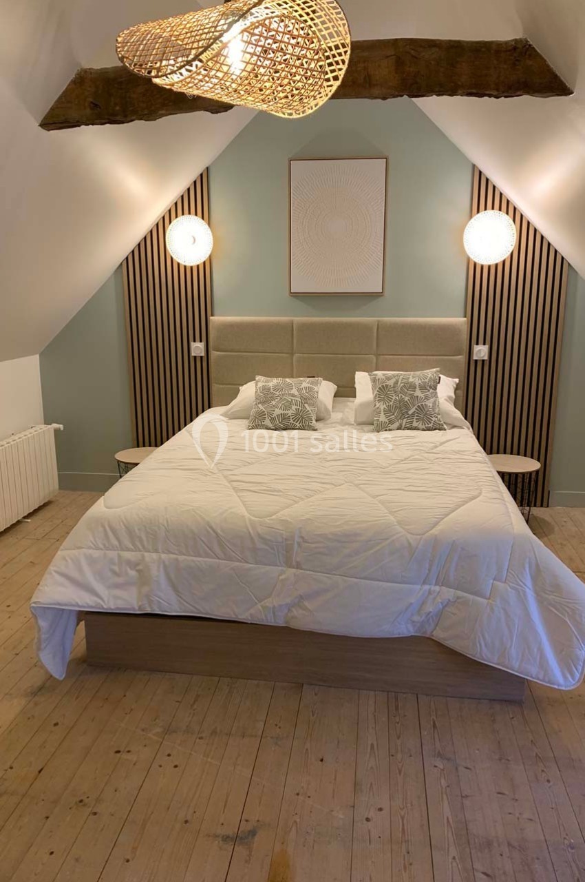 Chambre mansardée avec un lit double, des lampes murales rondes, un plafond en poutres apparentes et un parquet clair.