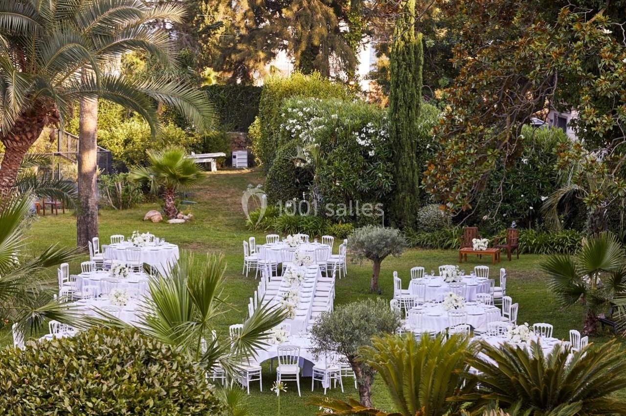 Tables et chaises blanches disposées dans un jardin verdoyant pour un événement en plein air.