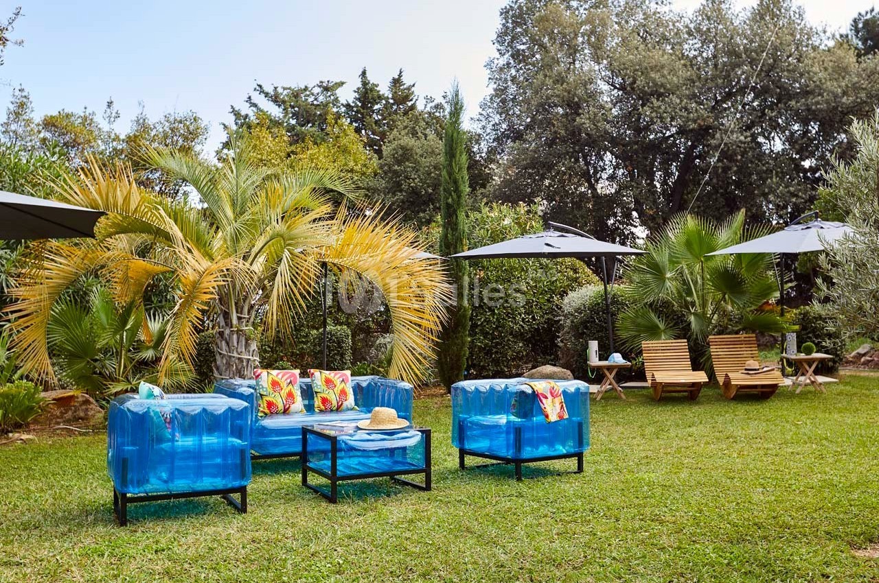 Mobilier de jardin coloré sur une pelouse entourée de végétation luxuriante, avec parasols et chaises longues en arrière…