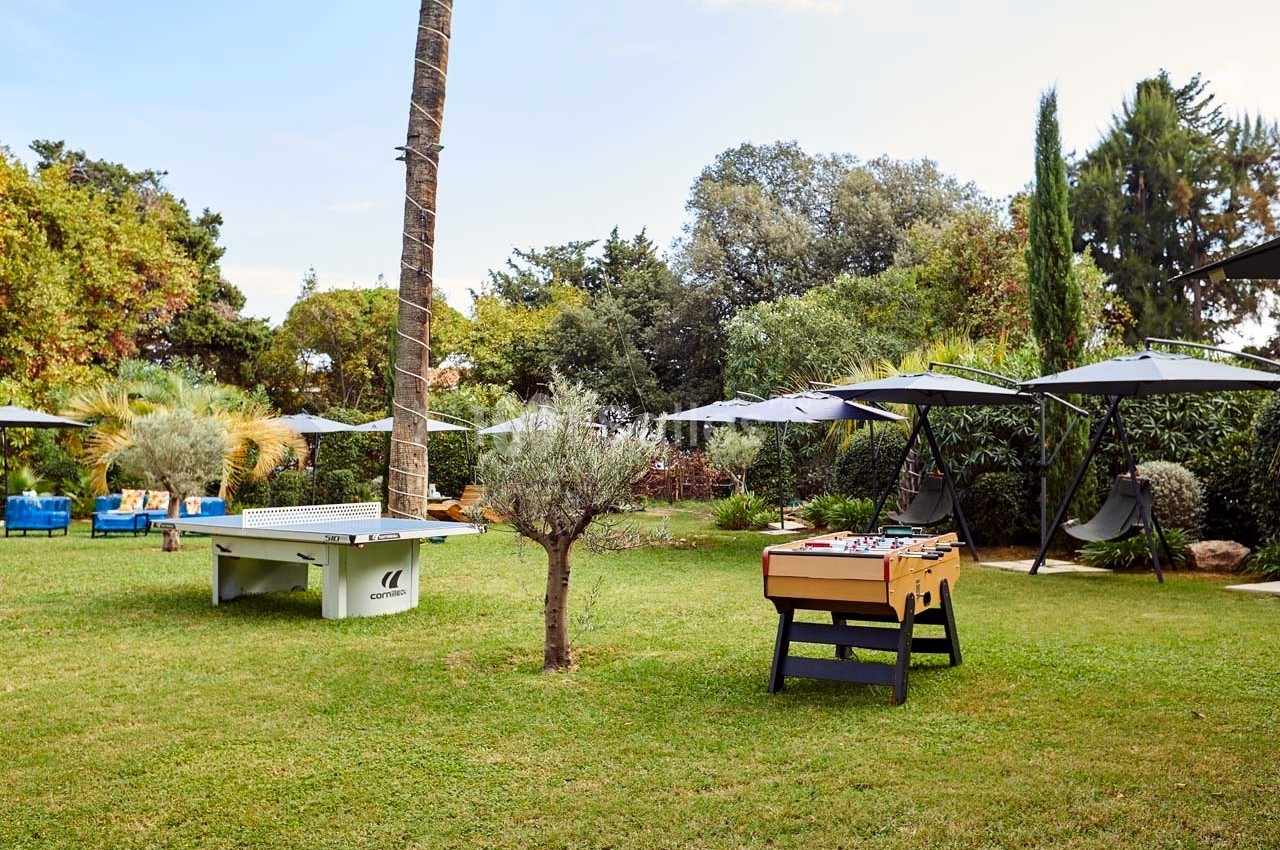 Jardin aménagé avec table de ping-pong, baby-foot, parasols, balançoires et végétation variée.