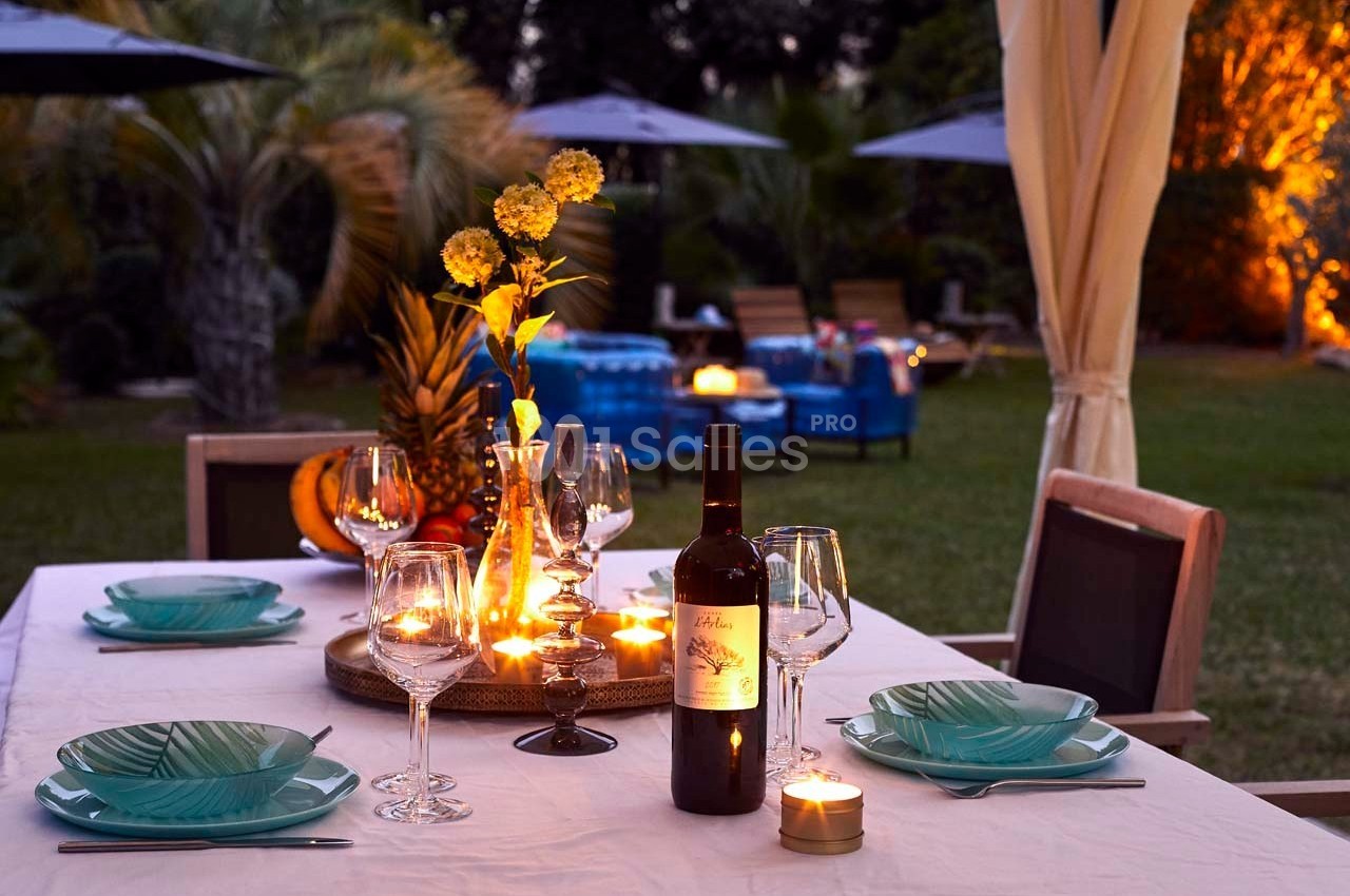 Table dressée en extérieur avec bougies, vaisselle élégante, bouteille de vin et décoration florale, ambiance chaleureuse.