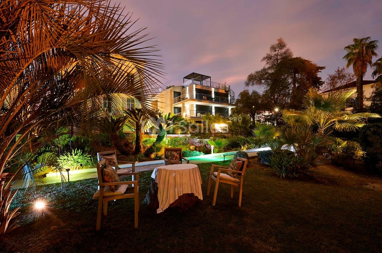 Jardin éclairé au crépuscule avec une table et des chaises au premier plan, et une maison moderne en arrière-plan.