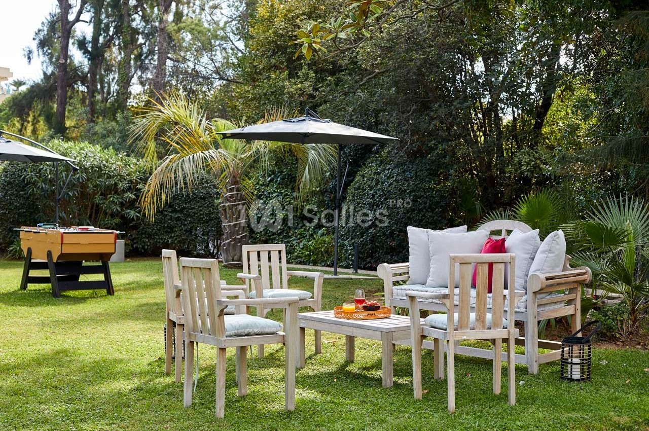 Mobilier de jardin en bois avec coussins, installé sur une pelouse, entouré de végétation et d'un baby-foot.