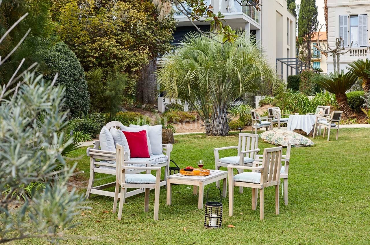 Mobilier de jardin en bois clair disposé sur une pelouse, entouré de végétation et d'arbustes.