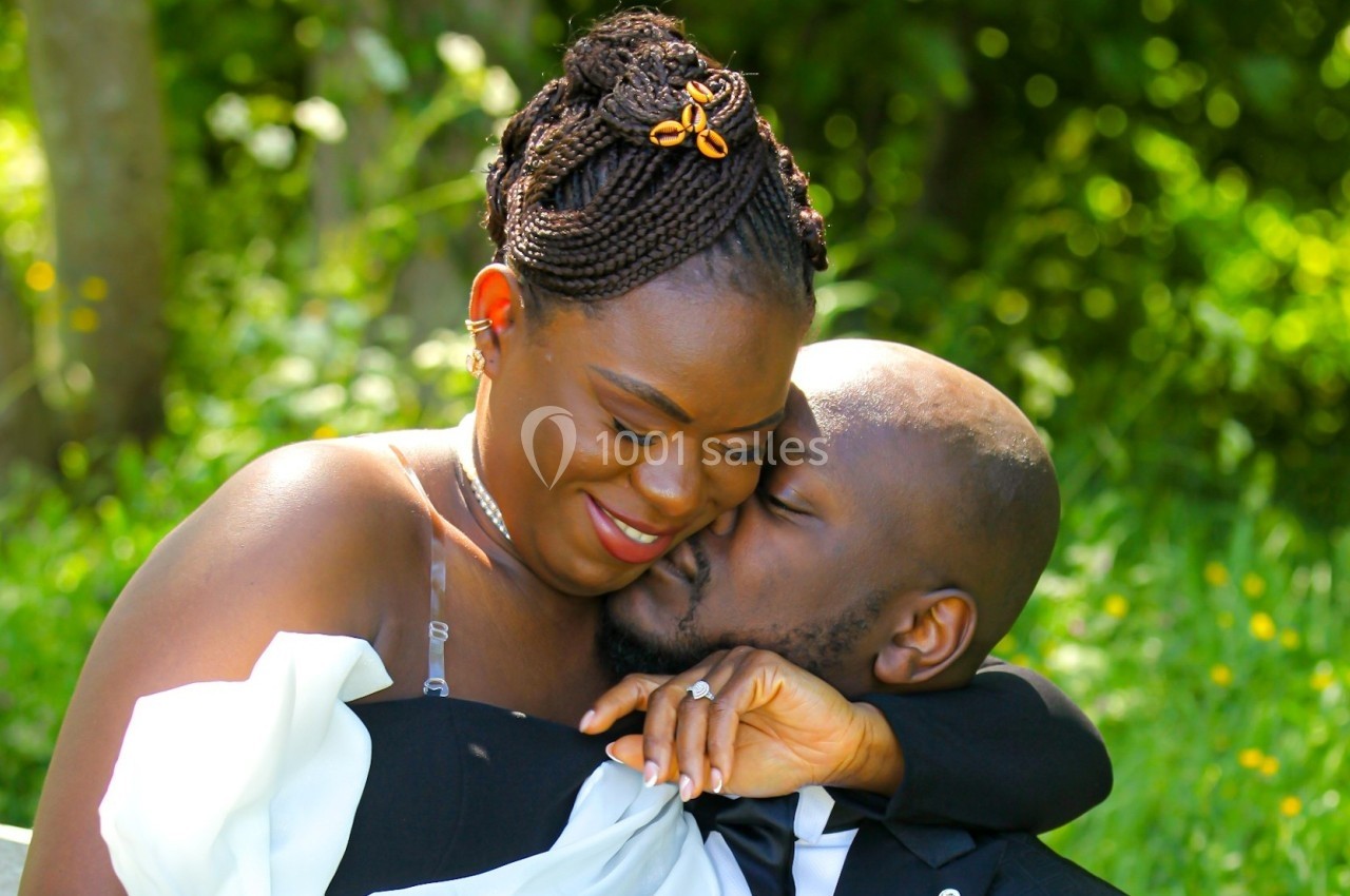 Un couple assis dans un jardin verdoyant, l'homme embrassant tendrement la joue de la femme souriante.