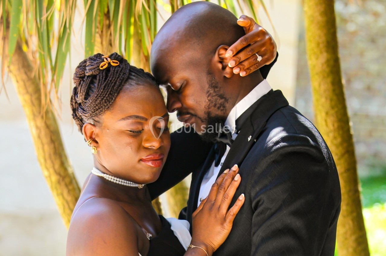 Un couple élégant partage un moment tendre sous un palmier, en tenue de soirée.