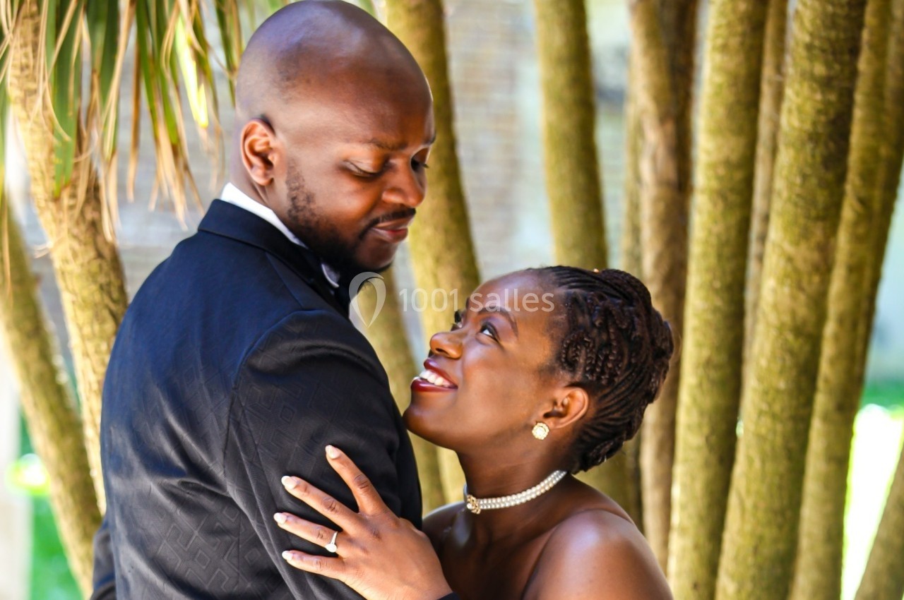 Un couple élégant échange un regard complice devant des troncs d'arbres dans un cadre naturel.