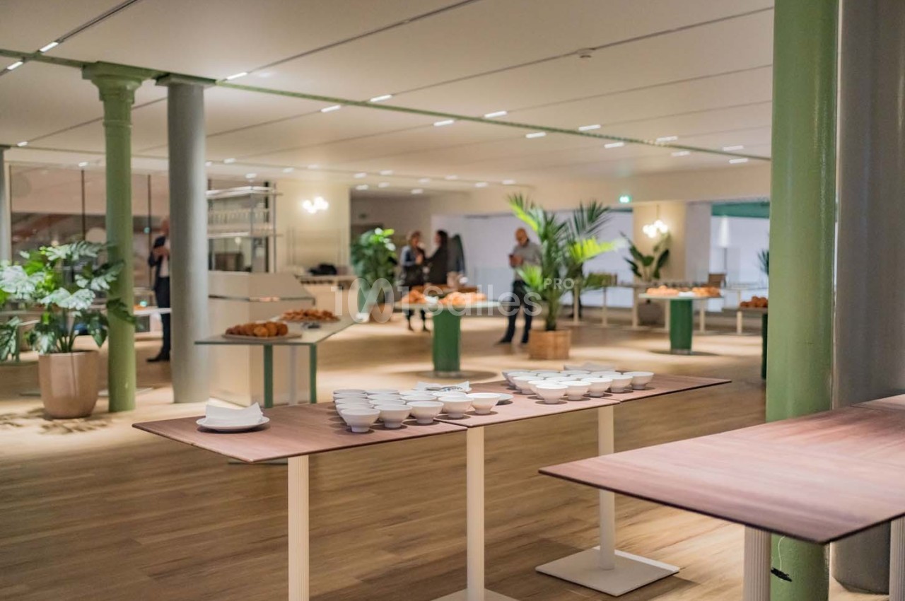 Salle lumineuse avec tables en bois, vaisselle blanche, viennoiseries et plantes décoratives en arrière-plan.