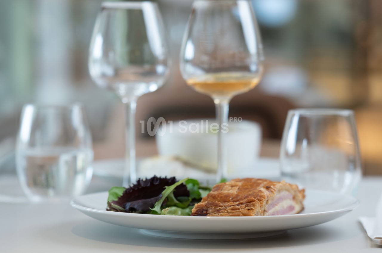 Assiette contenant une part de feuilleté et une salade verte, posée sur une table avec des verres vides et remplis.
