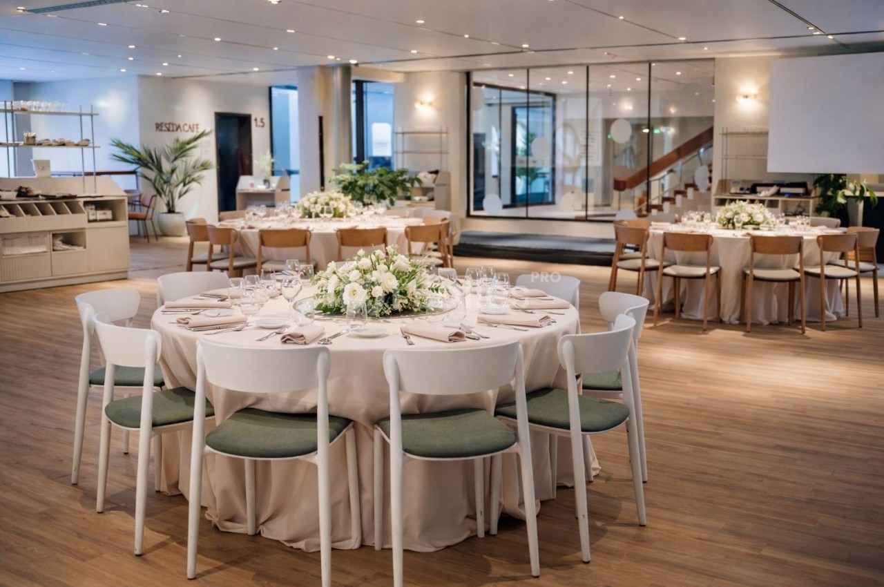 Salle de réception élégante avec tables rondes dressées, décorées de centres de table floraux et chaises blanches.