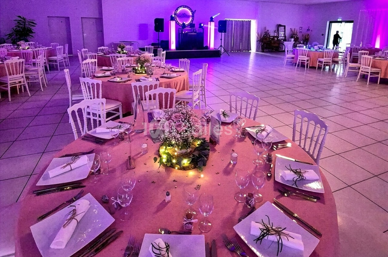 Salle de réception décorée avec des tables rondes élégamment dressées et éclairage d'ambiance violet.